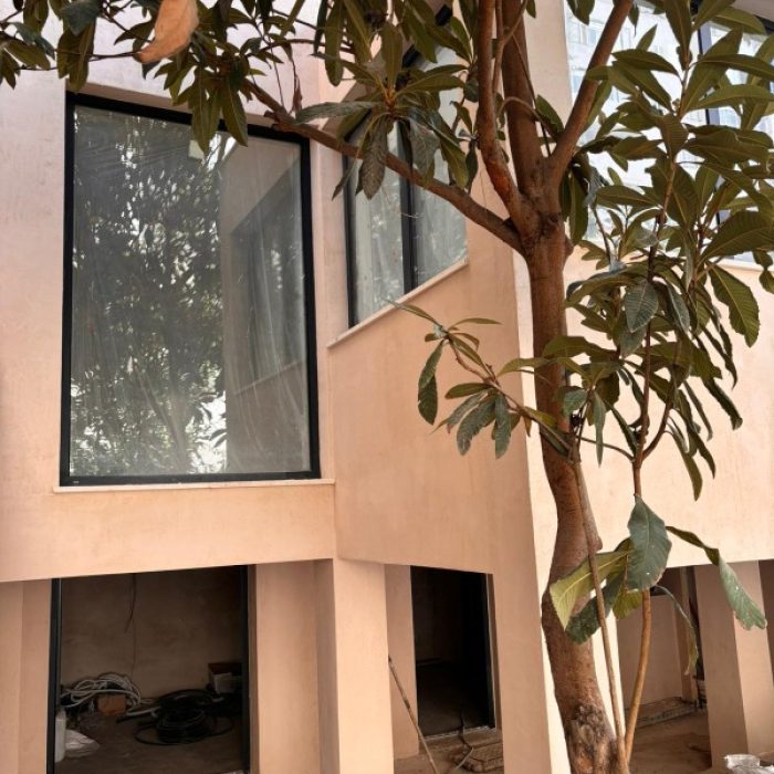 Minimalist modern villa exterior facade with a soft pinkish beige Chukum mineral coating behind a tree.