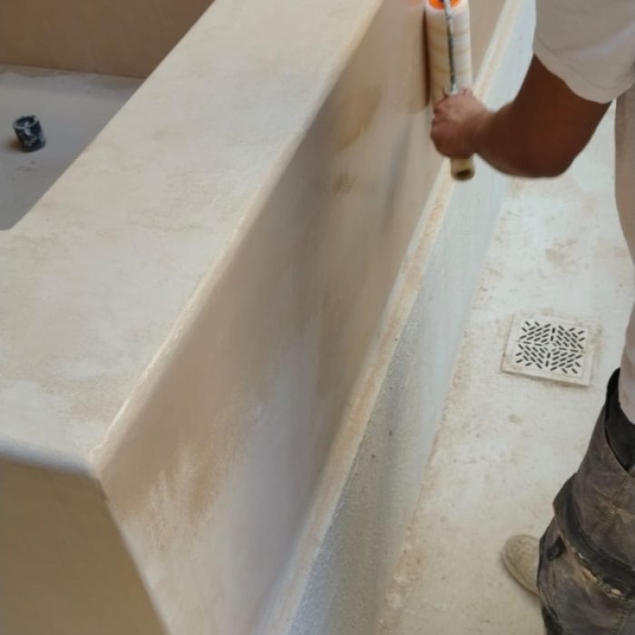 Artisan using a roller to apply a protective sealing coat to a smooth Chukum pool wall.